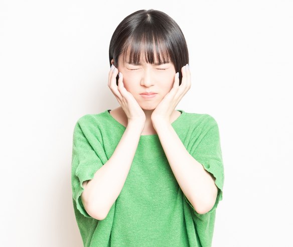強い歯の痛みで頬を押さえる女性